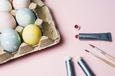 Paskalya yumurtalarını pastel suluboya renklerle boyama kavramı. Pembe arka planda Paskalya için yumurta boyamak için boya ve fırçalar.