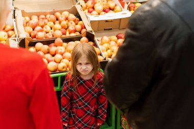 5 yaşında küçük bir kız anne ve babaya kötü bakıyor. Histerik bir kız, gözleri kapalı, ebeveynleri manipüle ederken yüksek sesle ağlıyor ve süpermarkette yemek tezgahının önünde duruyor..