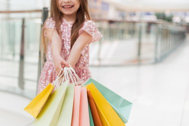 Küçük bir kız elinde rengarenk pastel poşetler tutuyor. Alışveriş merkezi konsepti, alışveriş merkezi. Yakın plan..