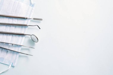 Dişçi aletleri: açık mavi arka planda tıbbi maskenin üzerinde duran ayna ve diş sondası. Reklam için desen.