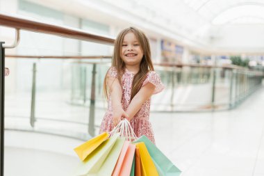 Küçük bir kız elinde rengarenk pastel poşetler tutuyor. Alışveriş konsepti, alışveriş merkezi..