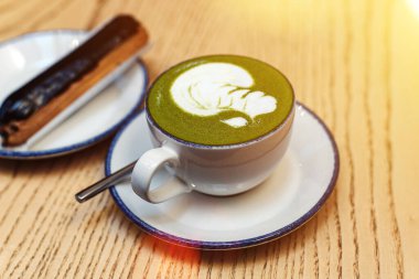 Kibrit yeşili, beyaz bardakta, bir kahve dükkanındaki ahşap masada, tatlı bir tatlının yanında. Kahvaltıda çikolatalı ekler..