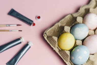 Paskalya yumurtalarını pastel suluboya renklerle boyama kavramı. Pembe arka planda Paskalya için yumurta boyamak için boya ve fırçalar