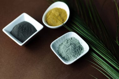 Siyah, sarı, gri kil beyaz bir porselen kasede kahverengi arka planda bir palmiye yaprağı ile. Ev ya da salon spa tedavisi için doğal kozmetik ürünleri, kopyalama alanı.