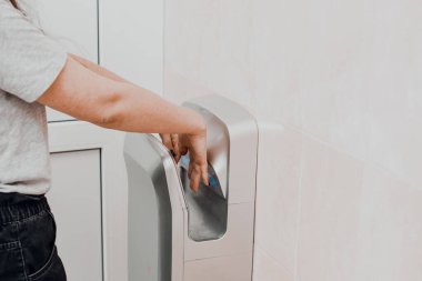 Halka açık bir yerde ellerini elektrikli kurutucuda kurutan bir kadın. Koronavirüs için önlem ve koruma.