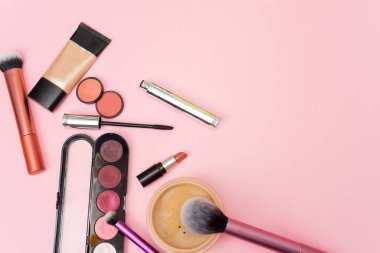 Gevşek yüz pudrası, fırça ve çeşitli göz farı, pembe arka planda allık ve rimel. Makyaj Ürünleri.