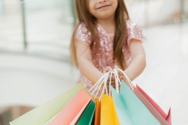 Küçük bir kız elinde rengarenk pastel poşetler tutuyor. Alışveriş merkezi konsepti, alışveriş merkezi. Yakın plan..
