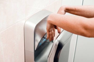 Halka açık bir yerde bir kadın ellerini elektrikli kurutucuda kurutuyor..