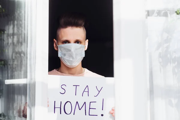 Young man in medical mask stay isolation at home for self quarantine. Concept home quarantine, prevention COVID-19, Coronavirus outbreak situation. Blank with the inscription: Stay at Home.