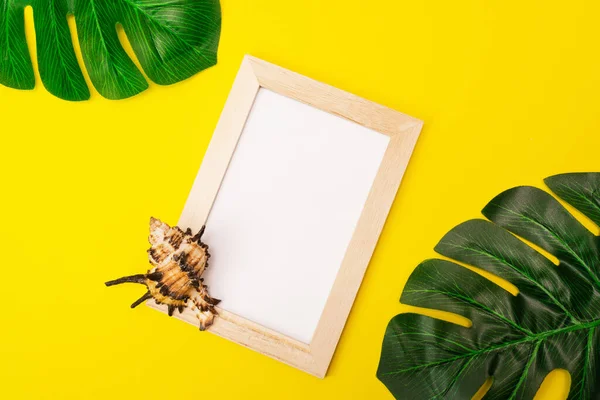 tropical mock up with white photo frame and palm leaves on colorful yellow background. Photo frame with empty place for text or advertisement with seashells on a yellow background.