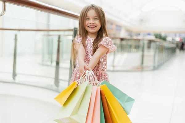 Happy girl holding shopping bags at the mall. A little girl holds multi-colored pastel bags in her hands close to the camera. The concept of shopping, shopping in the mall.