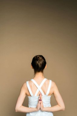 Bir kadın ellerini arkasından tutup bej bir arka planda yoga yapıyor. Genç ve güzel bir kız Parshvottanasana pozunda meditasyon yapıyor..