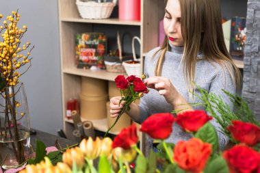 Çiçekçi kadın gül yapraklarını seçiyor. Sarışın, bir buket mükemmel kırmızı gül topluyor..