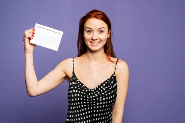 Kızıl saçlı bir kız gülümsüyor. Bir kızın beyaz bir çerçevesi var. Mor arka planda çekici bir kız. Reklamınız ya da mesajınız için ayarlayın.