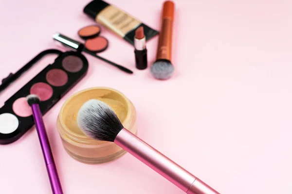 Loose face powder, brush and various cosmetic decorative makeup products on a pink background. Close up. Makeup brush and decorative cosmetics on a pastel pink background with copy space.