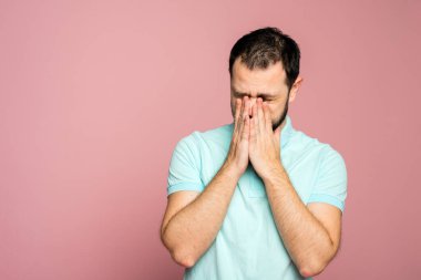 Mavi arka planda mavi tişörtlü bir adam elinde hapşırıyor. Eline hapşıramazsın, dirseğine ya da atkına hapşırmalısın. Kuralların ihlali.