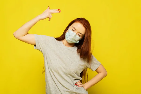 Una chica readhead está en máscara protectora sobre el fondo amarillo. Una chica está disparando. Una mujer quiere ser salva y saludable. Publicidad de máscara de seguridad. El virus puede matarte. — Foto de Stock