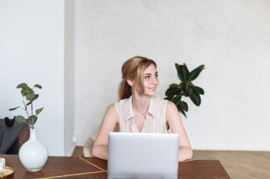 Genç bir bayan dizüstü bilgisayar kullanıyor, evdeki müşteriyle internet üzerinden iletişim kuruyor. Rahat ofis çalışma yeri, uzaktan çalışma, E öğrenme konsepti.