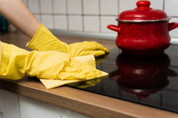 Someone is washing a kitchen stove in yellow gloves. Someone is cleaning a kitchen with rag.