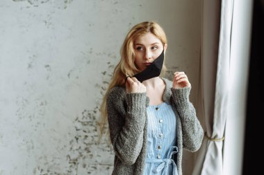 Genç bir kız dışarı çıkmadan önce kendi kendine koruyucu maske takıyor. Coronavirus salgını, karantina, evde kalın..