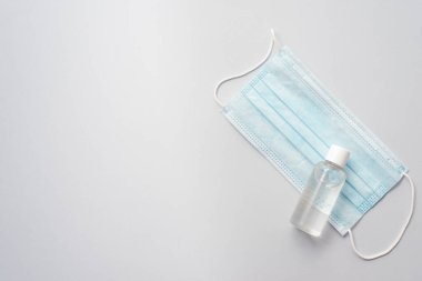 Plastik şişede jel dezenfektanı ve mavi arka planda koruyucu bir maske. Coronavirus koruması.