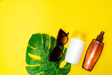 Güneş kremi, güneş gözlüğü sarı arka planda. Güneş koruma ürünleri sarı arka planda, yakın görüşte..