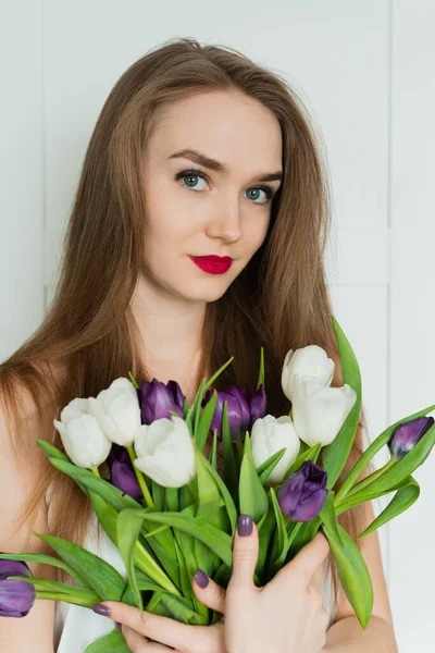 A beautiful girl is holding a big bouquet. A girl with a bouquet of tulips.