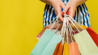 Bir kadın elinde farklı renkte alışveriş torbaları, kıyafetler ve taze kırmızı manikürlü çeşitli alışverişler tutuyor. Alışveriş, alışveriş ve satış kavramı. Kapatın. Web pankartı