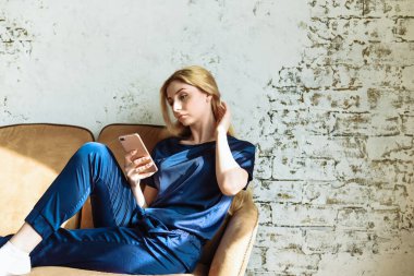 Ondan güzel bir mesaj. Çekici bir genç kadın akıllı telefonuna bakıyor ve evinde kanepede otururken gülümsüyor..