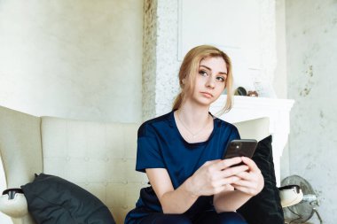 Evdeki koltukta otururken cep telefonu kullanan mutlu genç bir kadın..