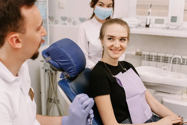 美しい少女が歯医者の椅子に座り 医者と助手の話を聞く 歯医者の予約と歯科医療 — ストック写真