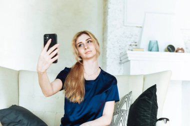 Evde kanepede otururken akıllı telefon kullanan çekici bir kadın. Telefon aracılığıyla alışveriş ve sosyal ağlar.