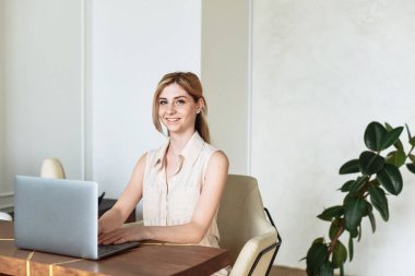 Genç bir bayan dizüstü bilgisayar kullanıyor, evdeki müşteriyle internet üzerinden iletişim kuruyor. Rahat ofis çalışma yeri, uzaktan çalışma, E öğrenme konsepti.