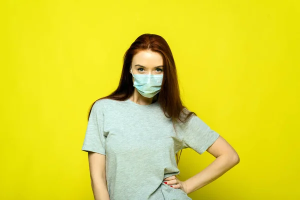 En kvinna klamrar sig fast vid huvudet och upplever rädsla, chock från spridningen av sjukdomen. Rödhårig vacker flicka i en skyddande mask på en gul bakgrund skriker från ett coronavirus — Stockfoto