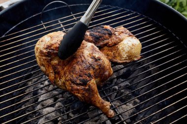 Bir çift maşa kömür ızgarasının üzerinde pişen tavuk parçasını kaldırır.