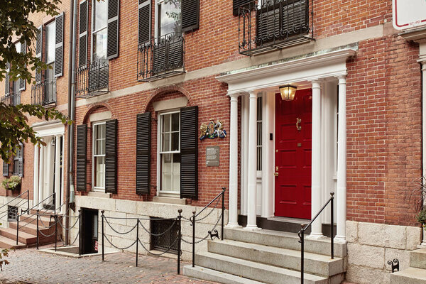 Boston, Massachusetts - October 3rd, 2019: Exterior of brownstone buildings with red door on Chestnut Street, in the historic Beacon Hill neighborhood of Boston