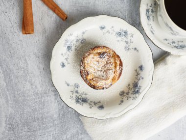 Taze pişmiş Portekiz usulü kremalı tart, Pasteis De Nata, bir fincan sıcak kahveyle birlikte porselen bir tabakta servis edilir.. 