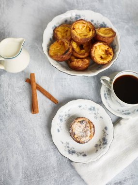 Taze pişmiş Portekiz usulü kremalı tart, Pasteis De Nata, bir fincan sıcak kahveyle birlikte porselen bir tabakta servis edilir.. 