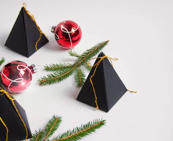 Uroczysty czarny prezent zawijania w formie piramid na białym tle z gałęziami choinki i czerwonymi dekoracjami świątecznymi. Widok poziomy — Zdjęcie stockowe