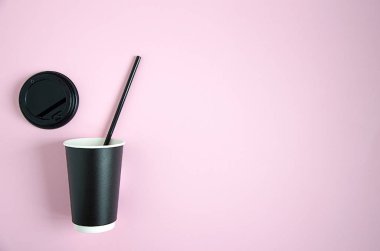 Kağıt bir kahve fincanı pembe arka planda yatıyor. Cama siyah bir kapak yerleştiriliyor. Bulanık ve yumuşak odak yatay görüntü doğal ışık