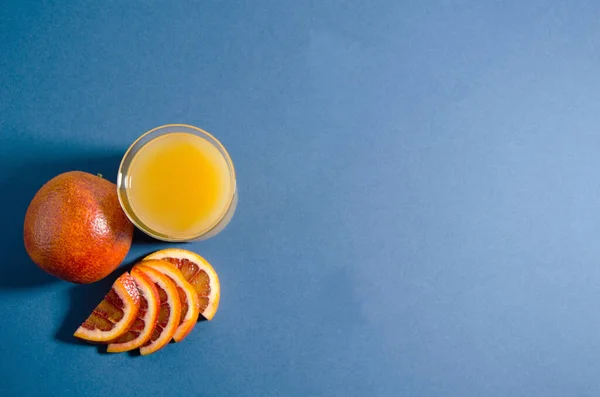 The whole red orange lies on a blue background. Slices of orange lie nearby and there is a glass of orange juice. Soft focus, top view. Trend blue background