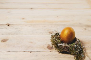 Paskalya geçmişi. Altın büyük yumurta, doğal ahşap arka planda, doğal bir kuş yuvasında yatay minimalist bir şekilde yatar.