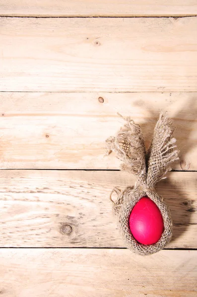 Easter bunny minimalist flat red chicken egg wrapped in burlap creative rabbit lies on a natural wooden background, top view, vertical background