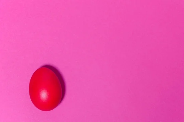 One colored Easter red egg lies on a pink background. Minimalistic background.
