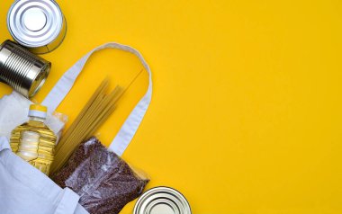 Paketlerdeki ürünler, şeker, karabuğday, makarna, şişedeki yağ ve ekolojik torba sarı arka planda. Gerekli ürünlerin karantina sırasında teslim edilmesi, kendi kendini izole etme. Kopyalama alanı.