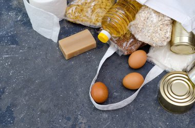 Karantina ve kendini izole etme süresince gerekli ürünlerin dağıtımı kavramı. Paketlerdeki ürünler şeker, karabuğday, makarna, şişedeki yağ, yumurta, sabun gri arka planda. Yatay görüntü. Kopyalama alanı.