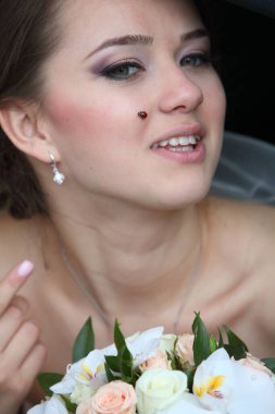 Elinde bir buket ve arka koltukta bir arabada yanağında bir uğur böceği olan bir gelin..