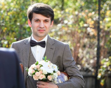 Ellerinde pembe çiçekli ve sulu bir düğün buketi olan damat.