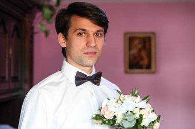 Beyaz gömlekli ve papyonlu damat elinde bir buket çiçekle.