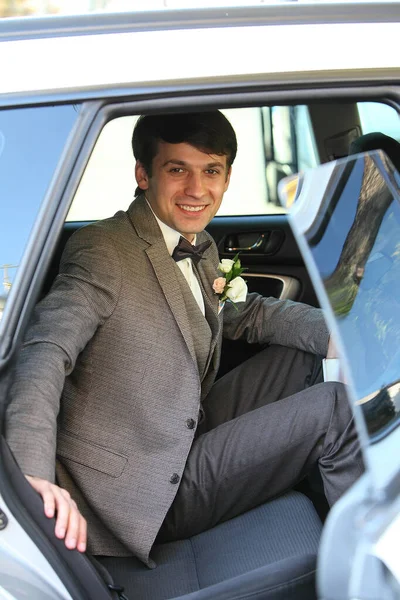 Pan młody w samochodzie na tylnym siedzeniu w szarym garniturze i uśmiechnięty — Zdjęcie stockowe